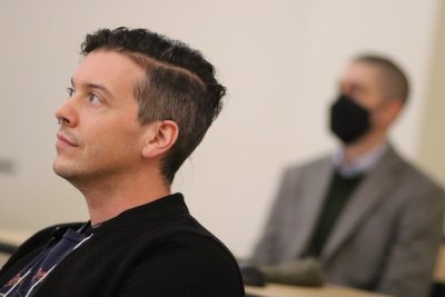 Ken Thompson (foreground; black shirt, no mask) and Andrew Ruis (blurred in background) listen to a presentation in an ITE classroom